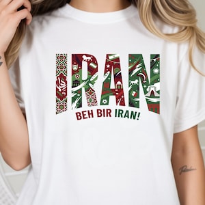 May include: White t-shirt with the word "IRAN" in a green and red design, featuring cultural symbols. The phrase "BEH BIR IRAN!" is printed below the word "IRAN".