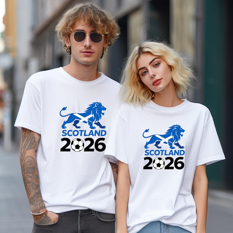 Pu&ograve; includere: T-shirt bianche con una grafica di leone blu, la bandiera scozzese, un pallone da calcio e la scritta "SCOTLAND 2026". Il disegno &egrave; centrato sul davanti delle magliette. Le magliette sono a maniche corte.