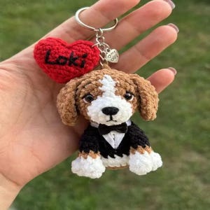 May include: A handmade crochet keychain featuring a beagle dog wearing a tuxedo and a red heart with the name "Loki". The dog has brown and white fur, a black bow tie, and white paws. A small charm reads "my dog".