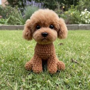 May include: A brown crochet poodle dog sits on green grass. The dog has a fluffy head and ears, with dark eyes and a small nose. The crochet work is detailed, creating a realistic and charming toy.