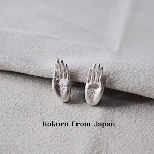 May include: Two silver-toned stud earrings, each in the shape of an open hand. The earrings have a textured finish and a small, circular detail at the palm. The text "Kokoro From Japan" is printed below the earrings.