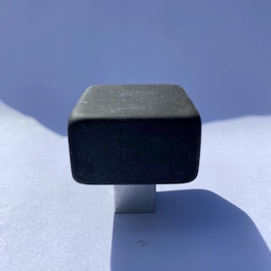 May include: A black square cabinet knob with a silver base.