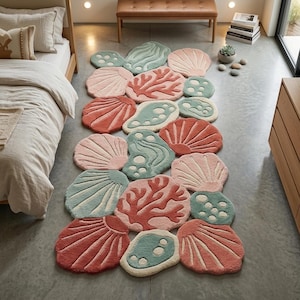Puede incluir: Una alfombra decorativa con diseño de temática marina. La alfombra presenta formas de conchas marinas y corales en tonos rosa, turquesa y coral. La alfombra está colocada sobre un suelo gris. El diseño de la alfombra es una adición caprichosa a cualquier habitación.