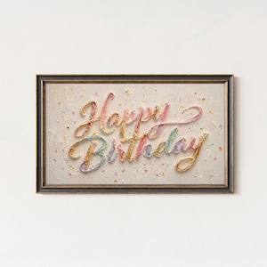 May include: A framed artwork with the words "Happy Birthday" in colorful, textured script. The text is in shades of pink, yellow, and blue, set against a speckled, off-white background. The frame is dark brown.