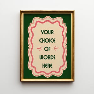 May include: A rectangular wall art print in a gold frame featuring a dark green background and a cream-coloured central scalloped label with pink borders. The text reads YOUR CHOICE OF WORDS HERE in dark green capital letters with small pink accents.