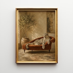 May include: A framed wall art print featuring a snow leopard resting on a rust-coloured velvet chaise lounge. Beside the furniture sits a potted olive tree in a textured terracotta vessel. The scene is set against a neutral wall with shadows.