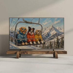 Könnte beinhalten: Gerahmter Kunstdruck mit drei Hunden in Skijacken und Sonnenbrillen auf einem Sessellift, mit schneebedeckten Bergen im Hintergrund. Das Kunstwerk wird auf einem Holzständer präsentiert. Das Bild zeigt eine Winterlandschaft.