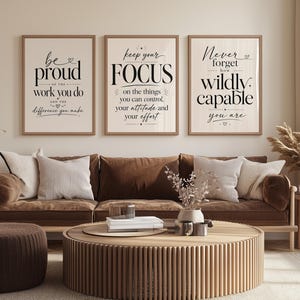 Op de afbeelding: Drie ingelijste wandkunstprints met inspirerende citaten: "Wees trots op het werk dat je doet", "Houd je focus" en "Vergeet nooit hoe wild capabel je bent". De prints worden boven een bruine bank getoond.