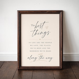 May include: A framed print with the words "The best things" in elegant script. The text continues with "In life are the people we love, the places we've been and the memories we've made along the way." The frame is dark brown.