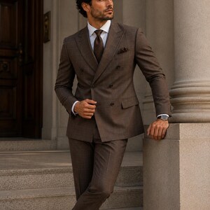 May include: A brown double-breasted suit with a subtle windowpane check pattern, worn with a crisp white collared shirt, a dark brown necktie, and a matching pocket square. The suit features structured shoulders, notched lapels, and dark buttons.