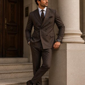 May include: A double-breasted brown suit with a subtle plaid pattern, worn with a crisp white collared shirt, a dark brown necktie, a pocket square, and dark brown leather dress shoes. The ensemble features a structured blazer and trousers.