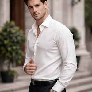 Puede incluir: Una camisa blanca con mangas largas y cuello cl&aacute;sico. La camisa est&aacute; abotonada y se combina con pantalones negros y un cintur&oacute;n negro. Se ve un reloj plateado en la mu&ntilde;eca.