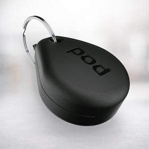 Può includere: Un portachiavi nero di forma ovale con la parola "pod" in rilievo sulla superficie. È attaccato a un portachiavi in metallo argentato. Lo sfondo è una sfumatura morbida e sfocata.