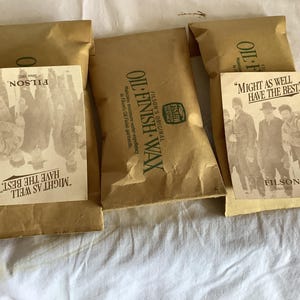 以下が含まれることがあります： Filsonオイルフィニッシュワックスの茶色の紙パッケージがいくつかあります。各パッケージには、「Might as well have the best」というテキストとFilsonのロゴが入ったヴィンテージスタイルのラベルが付いています。パッケージは白い表面に配置されています。