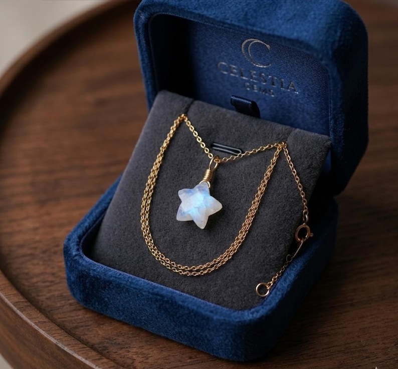 May include: A gold chain necklace with a star-shaped pendant, presented in a blue velvet jewelry box. The pendant is a light blue and white gemstone. The jewelry box has the text "CELESTIA GEMS" printed on the inside of the lid.