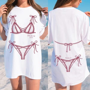 May include: White t-shirt featuring a burgundy lingerie design on the front and back. The front design includes a bra and panties with the text "Palm Springs 2026". The back design includes a thong and the word "Bridesmaid".