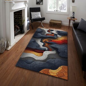 Könnte beinhalten: Ein rechteckiger Teppich mit einem abstrakten Design aus fließenden Linien und einer Farbpalette aus Dunkelblau, Grau, Weiß, Orange und Gelb. Der Teppich liegt auf einem Holzboden in einem Wohnzimmer.