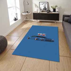 May include: A rectangular blue rug featuring a stylized illustration of a blue sports car with the letters "GTR" in red and white. The rug is placed on a wooden floor in a room with a window and furniture.