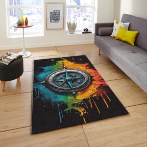 May include: A rectangular area rug featuring a compass design. The compass is centered on a black background with a colorful, abstract map-like design in shades of blue, green, orange, and yellow. The rug is placed on a wooden floor.