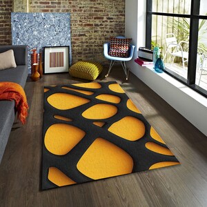 May include: A modern area rug with a unique design. The rug features a black background with large, irregular, yellow shapes. The rug is placed on a wooden floor in a living room setting. The rug's design adds a contemporary touch to the room's decor.