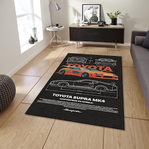 May include: Black rectangular rug featuring a detailed illustration of a Toyota Supra MK4. The design includes the car's outline, technical drawings, and the text "TOYOTA SUPRA MK4 - MASTERPIECE ON WHEELS". The car is orange and blue.