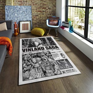 以下が含まれることがあります： 白黒のマンガ風イラストが描かれた長方形のラグ。ラグには「VINLAND SAGA」の文字と、キャラクターと群衆の詳細な画像が描かれています。追加のテキストと制限付きの評価が含まれています。