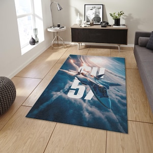 May include: Rectangular area rug featuring a fighter jet soaring through a cloudy sky. The jet is blue and gray, with the number "5X" in large white letters. The rug has a blue and white color scheme.
