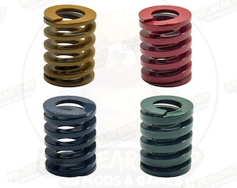 May include: Four coil springs in gold, red, navy blue, and green. Each spring is cylindrical with a flat top and bottom, and the coils are evenly spaced. The springs are likely for mechanical or industrial use.