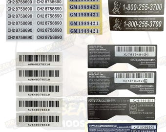 May include: A collection of rectangular adhesive labels featuring various serial numbers, barcodes, and technical information for electronic devices. The set includes white labels with black text, silver labels with blue text, and black labels with white text.