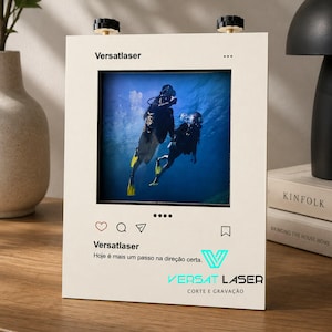 Pode incluir: Moldura creme com foto de dois mergulhadores em água azul. A moldura tem botões pretos na parte superior e ícones e texto no estilo de mídia social, incluindo "Versatlaser" e "Hoje é mais um passo na direção certa."
