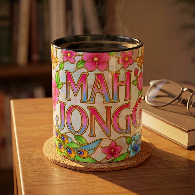 A ceramic mug with a black handle and interior, featuring the phrase "Mah Jongg" in a stained glass aesthetic.