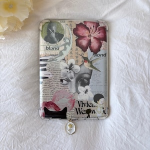 May include: Clear phone case with a collage design featuring floral and artistic elements. The case includes a pendant with a white and gold flower charm. The design incorporates text and a black cat silhouette.