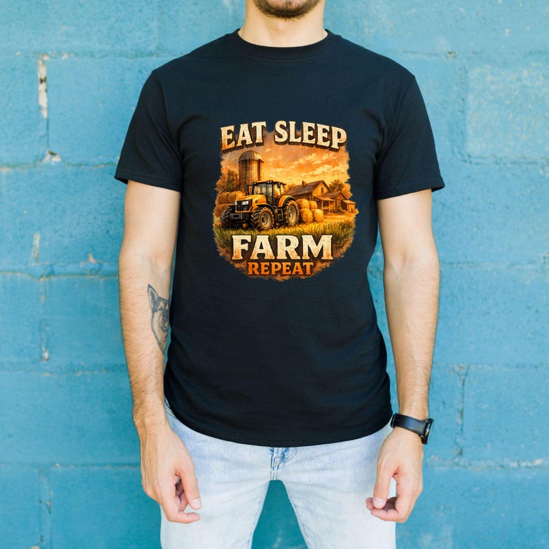 May include: A black short-sleeved t-shirt featuring a graphic print of a yellow tractor in a field with hay bales at sunset. The text EAT SLEEP FARM REPEAT is printed in a bold, distressed font above and below the central farm scene illustration.