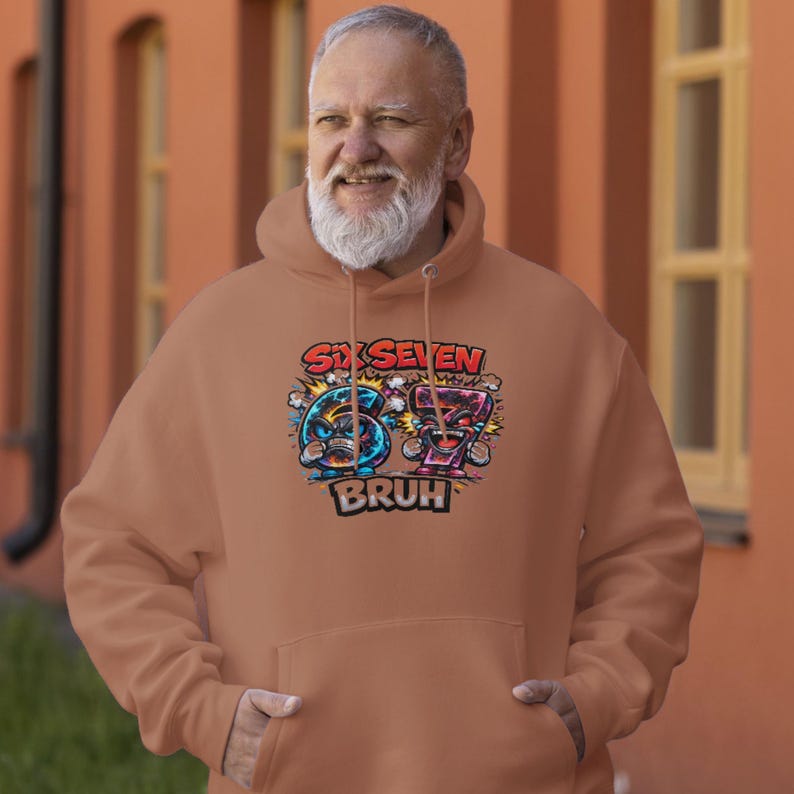 May include: A tan hoodie with a graphic design featuring the words "Six Seven" above the numbers 6 and 7, each with cartoon faces. Below the numbers is the word "BRUH". The hoodie has a hood and a front pocket.