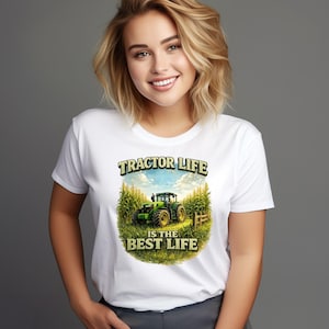 May include: A white short-sleeved t-shirt featuring a graphic print of a green tractor in a cornfield. The text above the tractor reads TRACTOR LIFE and the text below reads IS THE BEST LIFE. The design is centered on the front of the shirt.