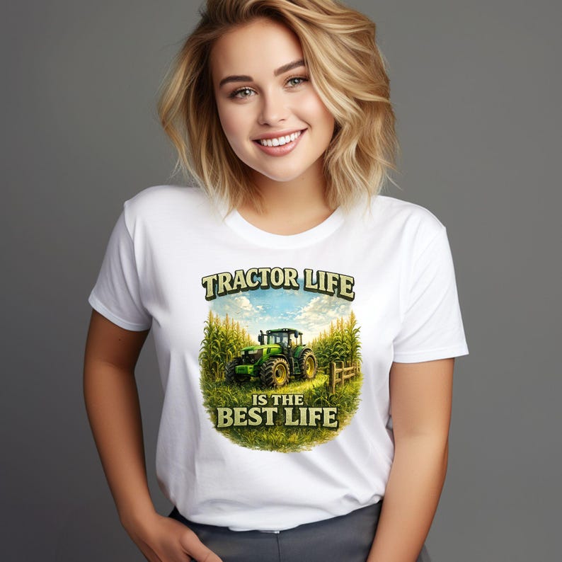 May include: A white short-sleeved t-shirt featuring a graphic print of a green tractor in a cornfield. The text above the tractor reads TRACTOR LIFE and the text below reads IS THE BEST LIFE. The design is centered on the front of the shirt.