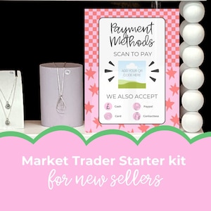 May include: A display featuring jewelry and a sign with payment methods. The sign is pink with a checkered pattern and star accents, listing accepted payment types. A silver necklace with a teardrop pendant is visible.