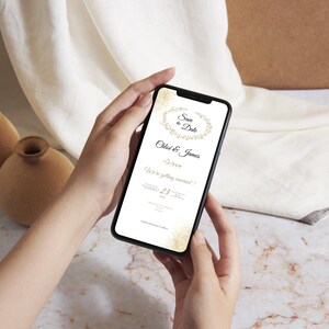 May include: A smartphone screen showing a digital wedding invitation. The invitation includes the text "Save the Date" and the names "Chloe & James", with a floral wreath design. The date is the 23rd.