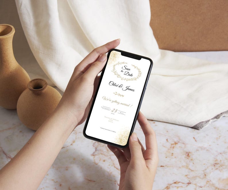 May include: A smartphone screen showing a digital wedding invitation. The invitation includes the text "Save the Date" and the names "Chloe & James", with a floral wreath design. The date is the 23rd.