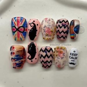 May include: A collection of ten false nails, each with unique designs. The designs include a Union Jack with an infinity symbol, black paisley on pink, floral patterns with gold studs, and a zigzag pattern. One nail reads "Keep Calm and" with a mustache.