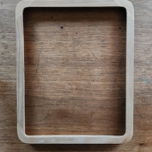 May include: A light-colored, rectangular wooden tray with rounded corners. The tray is empty and sits on a wooden surface. The tray's design is simple and modern, suitable for serving or display.