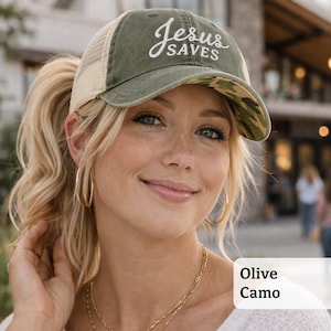 Light pink women’s Christian trucker hat with white embroidered “Jesus Saves” text, two toned hat. Styled on a smiling woman with curly ponytail in front of a modern church. Vintage washed unstructured ponytail baseball cap with feminine floral details and faith-inspired boutique style.