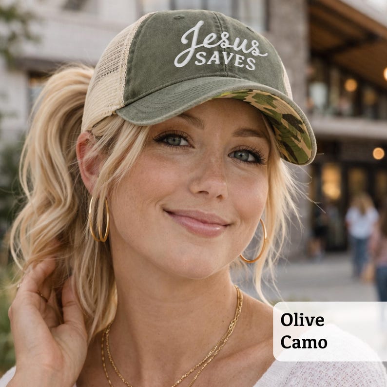 Light pink women’s Christian trucker hat with white embroidered “Jesus Saves” text, two toned hat. Styled on a smiling woman with curly ponytail in front of a modern church. Vintage washed unstructured ponytail baseball cap with feminine floral details and faith-inspired boutique style.