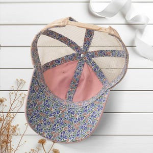Light pink women’s Christian trucker hat with white embroidered “Jesus Saves” text, two toned hat. Styled on a smiling woman with curly ponytail in front of a modern church. Vintage washed unstructured ponytail baseball cap with feminine floral details and faith-inspired boutique style.