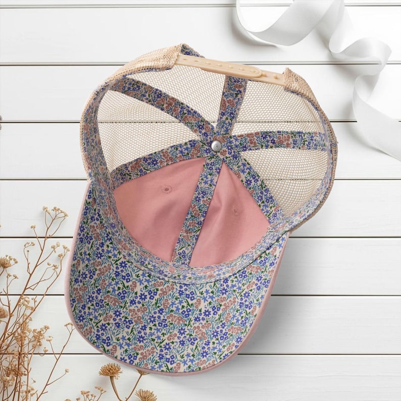 Light pink women’s Christian trucker hat with white embroidered “Jesus Saves” text, two toned hat. Styled on a smiling woman with curly ponytail in front of a modern church. Vintage washed unstructured ponytail baseball cap with feminine floral details and faith-inspired boutique style.