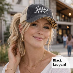 Light pink women’s Christian trucker hat with white embroidered “Jesus Saves” text, two toned hat. Styled on a smiling woman with curly ponytail in front of a modern church. Vintage washed unstructured ponytail baseball cap with feminine floral details and faith-inspired boutique style.