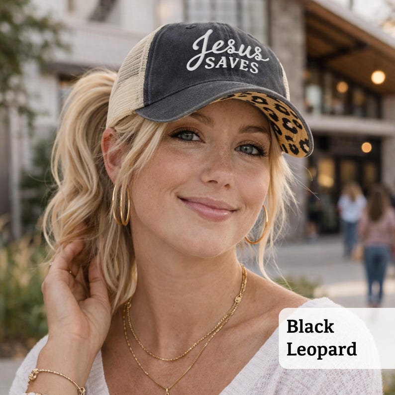 Light pink women’s Christian trucker hat with white embroidered “Jesus Saves” text, two toned hat. Styled on a smiling woman with curly ponytail in front of a modern church. Vintage washed unstructured ponytail baseball cap with feminine floral details and faith-inspired boutique style.