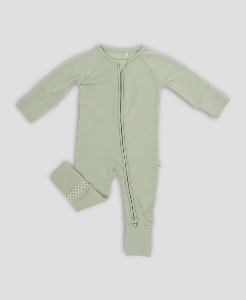 K&ouml;nnte beinhalten: Hellgr&uuml;ner Baby-Schlafanzug mit durchgehendem Rei&szlig;verschluss und langen &Auml;rmeln. Die Fu&szlig;b&uuml;ndchen haben ein wei&szlig;es Tupfenmuster. Der Schlafanzug ist aus einem weichen, bequemen Material gefertigt.