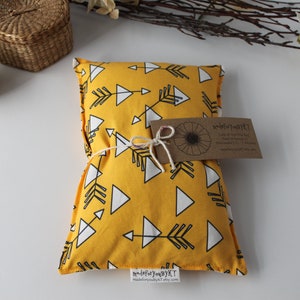 May include: A yellow fabric heat pack with a white arrow and triangle pattern. The heat pack is tied with twine and has a brown paper tag that reads "Made for You by KT" and "Cold or Hot Therapy Bag".