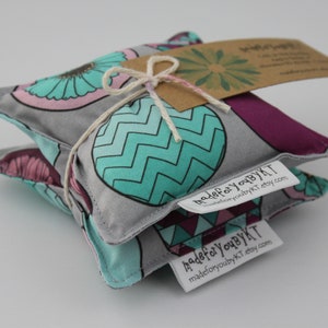 May include: A gray and teal fabric hot pack with a geometric pattern. The hot pack is tied with twine and has a brown paper tag that says "madeforyoubyKT" and a website address.